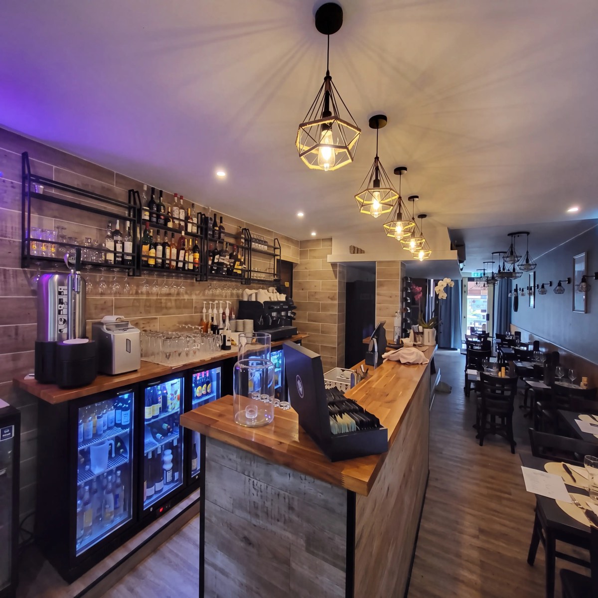 La salle du restaurant : bar en bois, suspensions et tables dressées